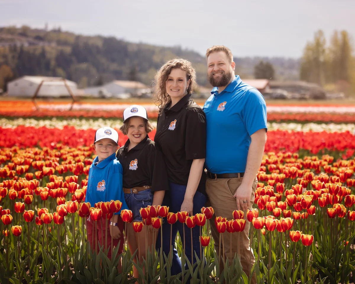 Family-owned farm business owners posing in red and yellow tulip field with greenhouses in background